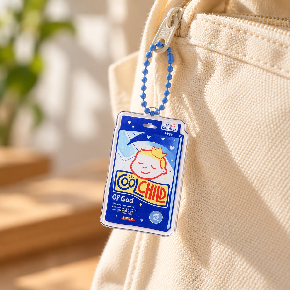 Cool Child of God fever patch acrylic keychain hanging from a cream canvas bag in warm natural light.