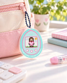 Digital Pet Nurture Your Faith acrylic keychain attached by a navy ball chain to a pink zipper on a cream-and-pink pouch.