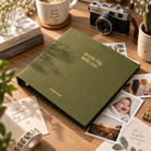 Dream Big Little One green planner styled with a camera and printed photos on a wooden desk