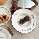 White ceramic plate with the words "God loves you every day" and "Dreams sprout because of God," served with chocolate pastries, surrounded by breakfast items and a cozy setting, inspiring faith and simple happiness.