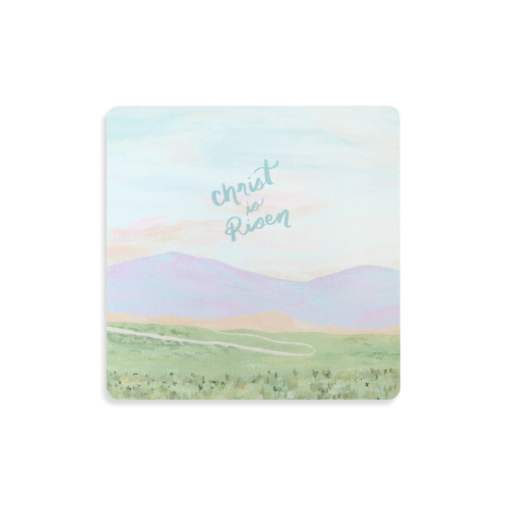 Christian-themed coaster with pastel landscape art and the message 'Christ is Risen,' perfect for Easter and faith-inspired home decor.