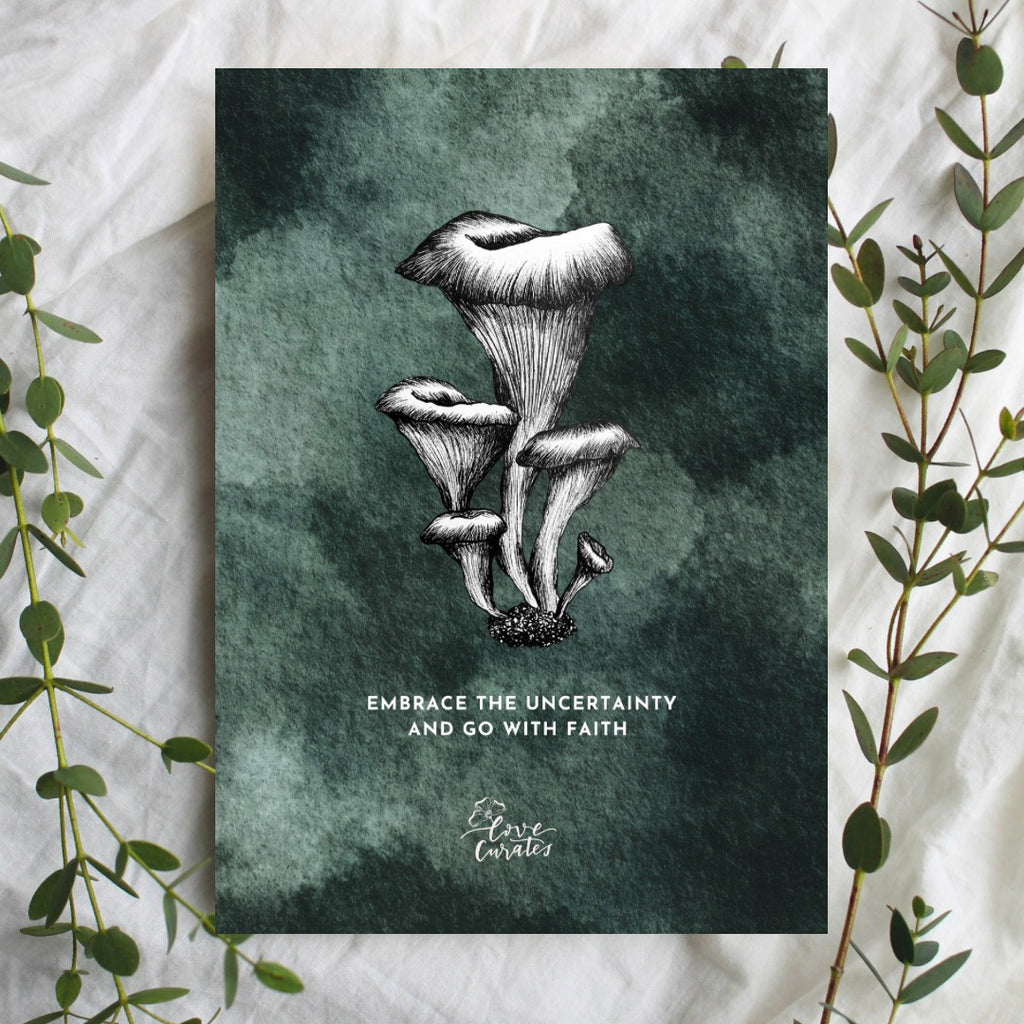 A greeting card featuring a black and white illustration of mushrooms on a dark green textured background. The card displays the message 'Embrace the uncertainty and go with faith,' symbolizing resilience and faith. Green foliage frames the edges of the card.