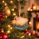 Emmanuel baby Jesus manger Christmas ornament hanging on a tree with warm fairy lights