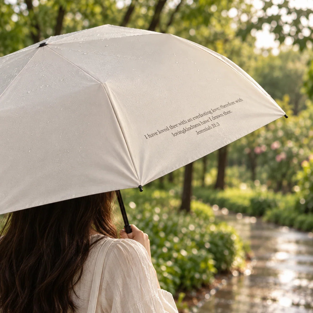 Cream scripture umbrella opened on a green park path, held by a person outdoors.