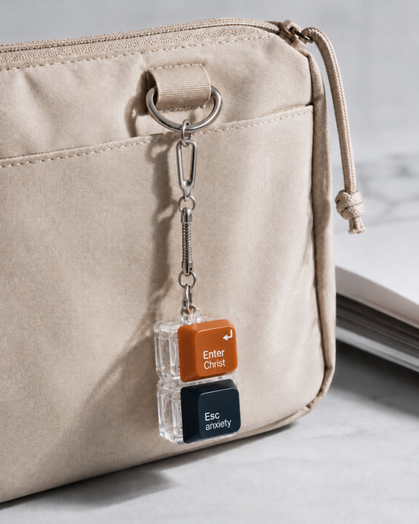 Enter Christ Esc anxiety light-up keycap keychain clipped to a beige bag