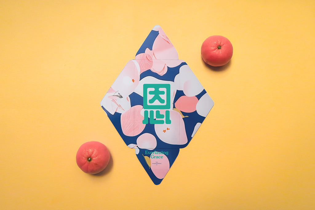 Chinese New Year red packet with 'Everlasting Grace' theme, showcasing blue abstract designs with peach motifs and a bold green Chinese character, placed alongside tangerines on an orange background.