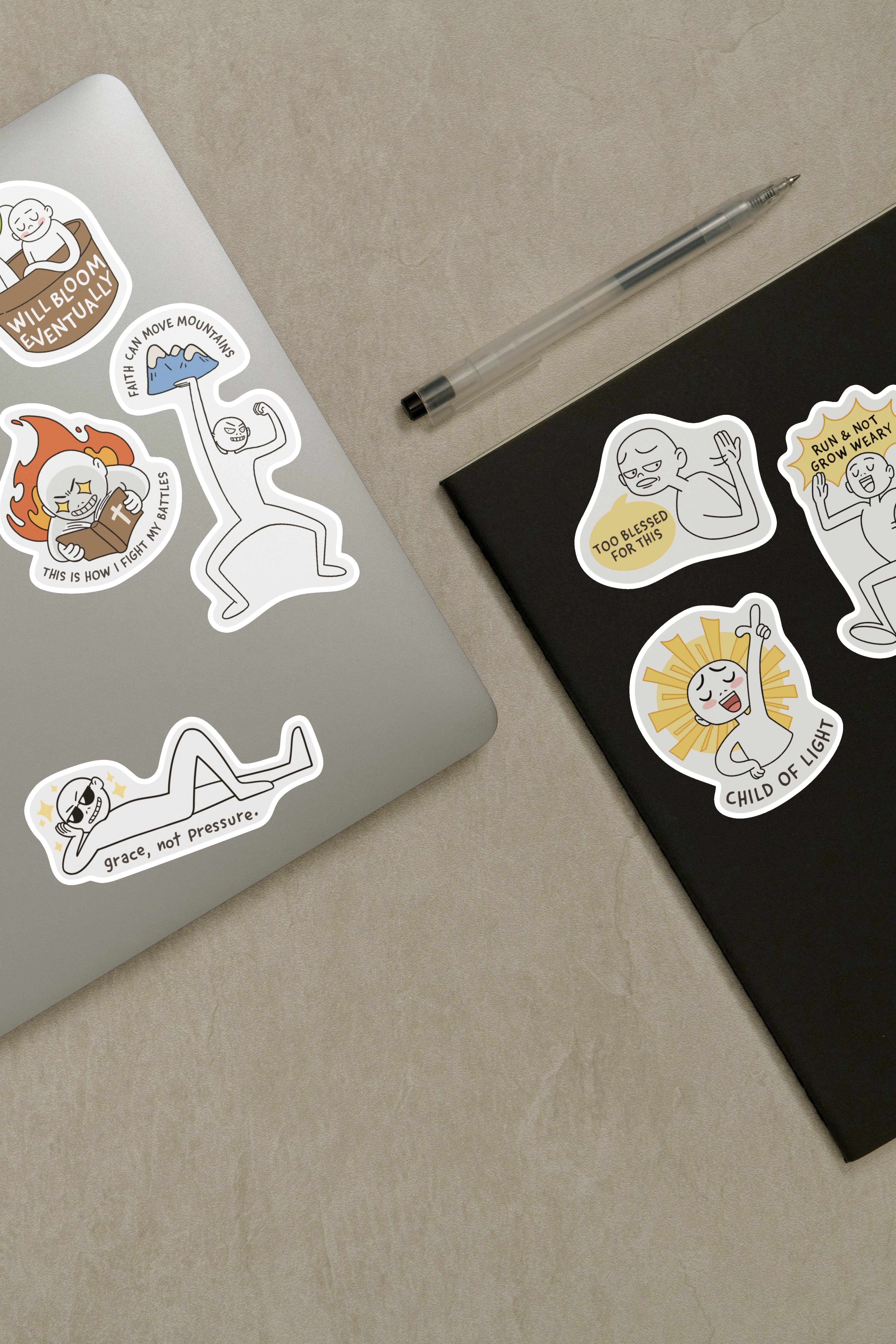 Laptop and notebook adorned with Everyday Believer stickers featuring Christian messages like "Grace, Not Pressure" and "Child of Light," from The Commandment Co, Singapore.