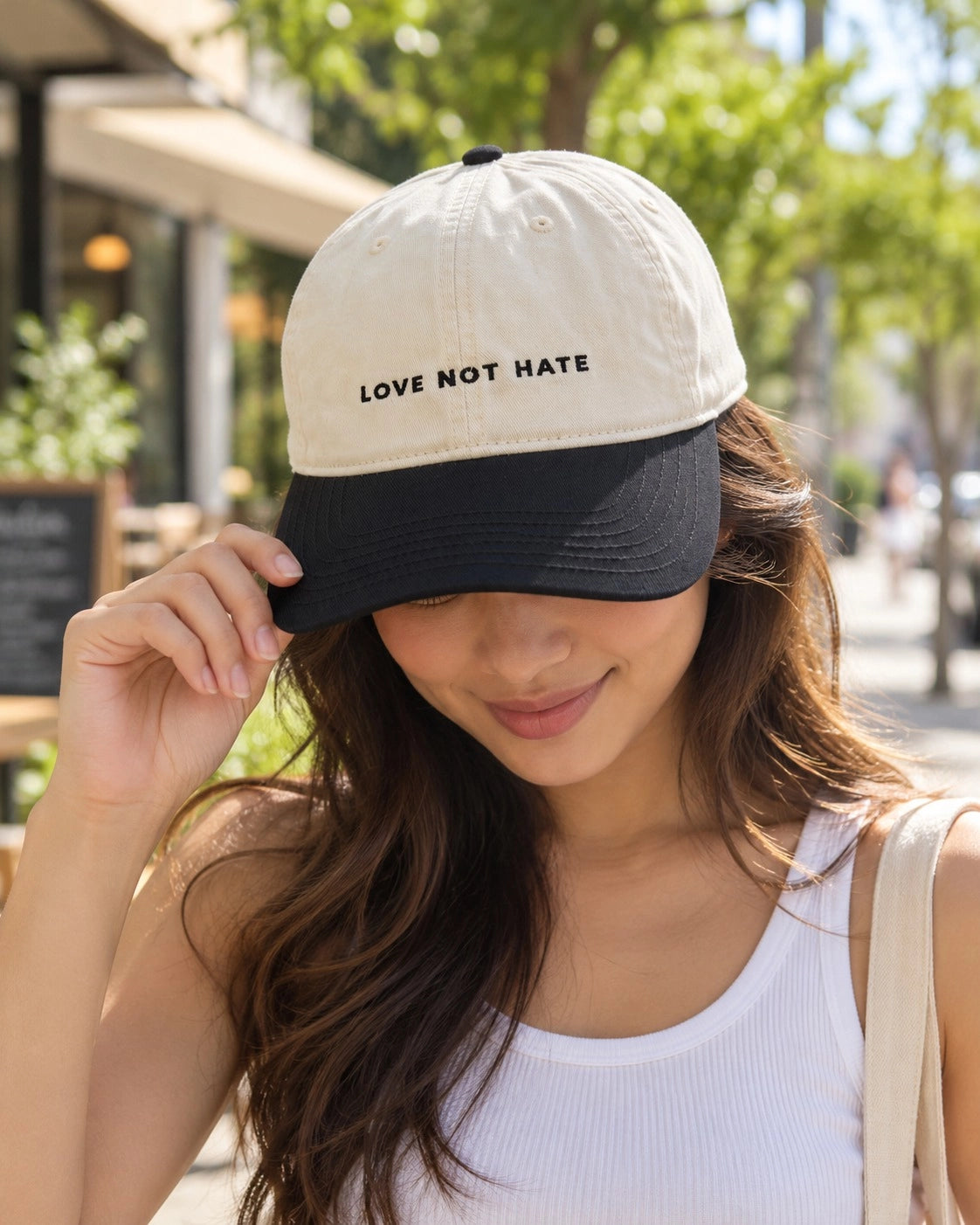 Everyday Truths cream and navy baseball cap with Love Not Hate embroidered lettering worn outside.
