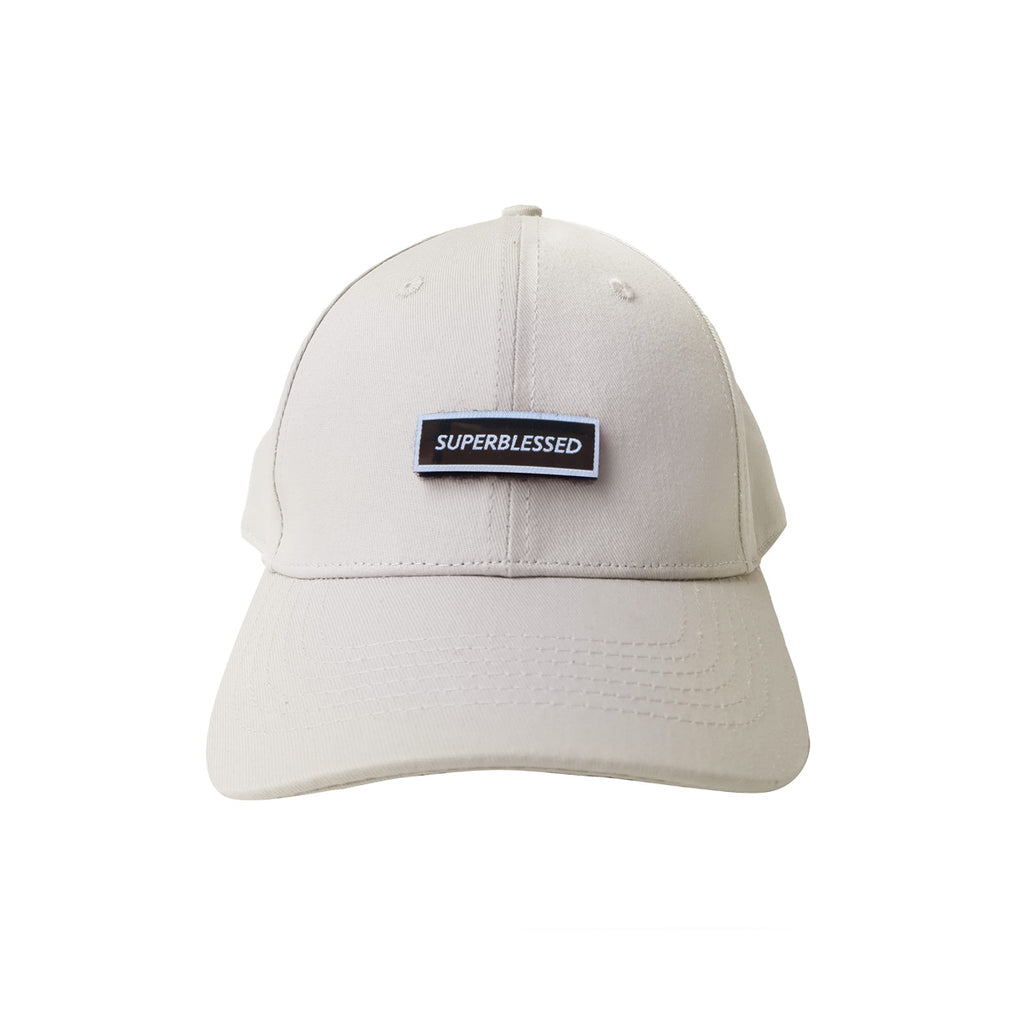 A beige cap with a black patch embroidered with the word "SUPERBLESSED," designed as a stylish Christian streetwear accessory.