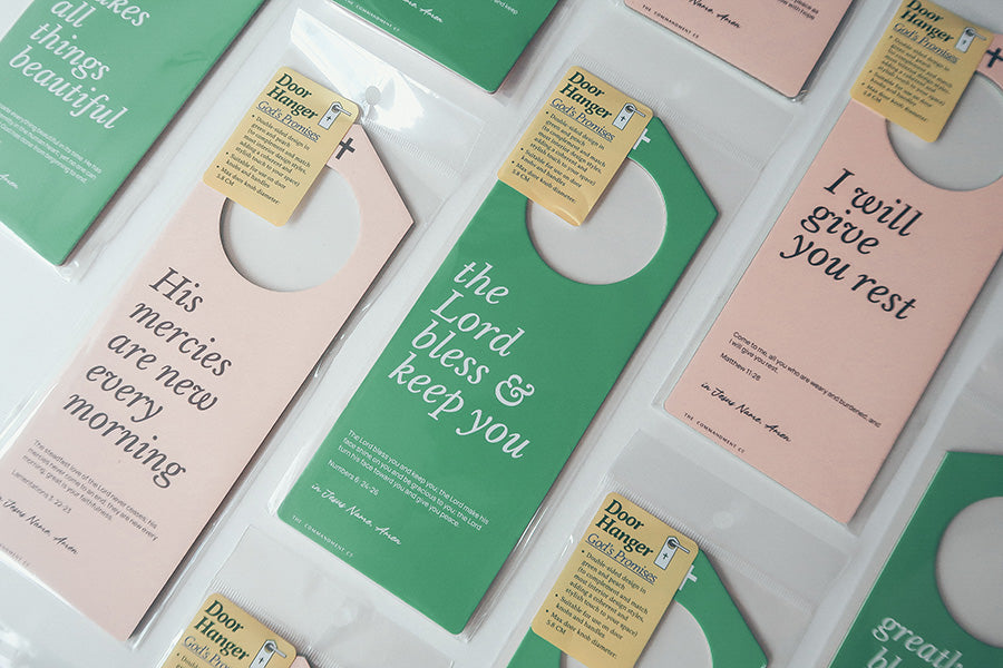 Assorted Christian door hangers with Bible verses such as 'His mercies are new every morning,' 'The Lord bless & keep you,' and 'I will give you rest,' displayed in packaging with tags highlighting 'God's Promises.'