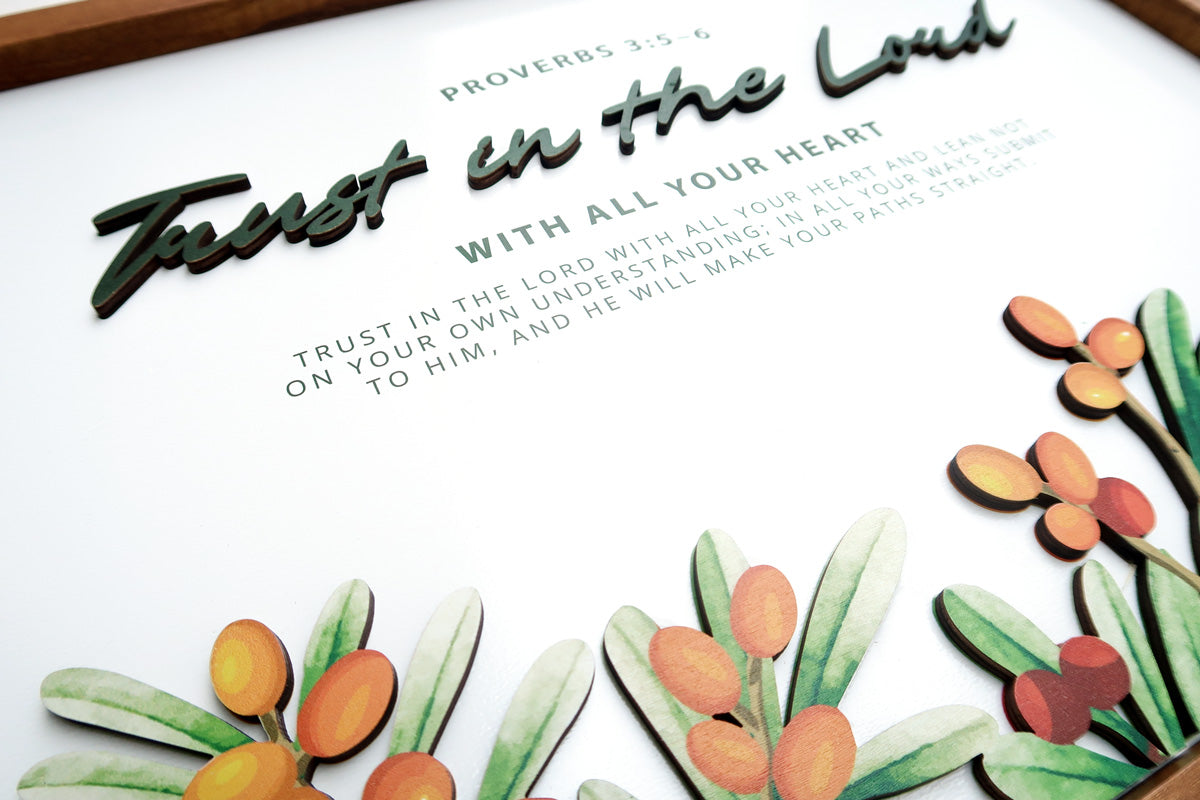 Close-up of a wooden board poster featuring the scripture "Trust in the Lord with all your heart" from Proverbs 3:5-6. The design includes layered text and decorative orange berries with green leaves.