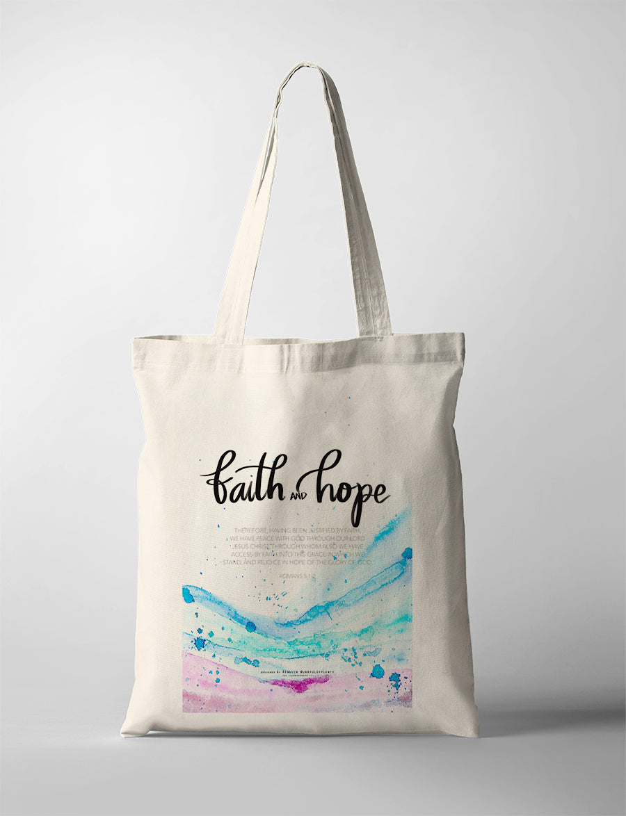 Christian tote bag with watercolor blue and pink waves and the words ‘Faith and Hope’, inspired by Romans 5:1–2 about peace with God through faith.