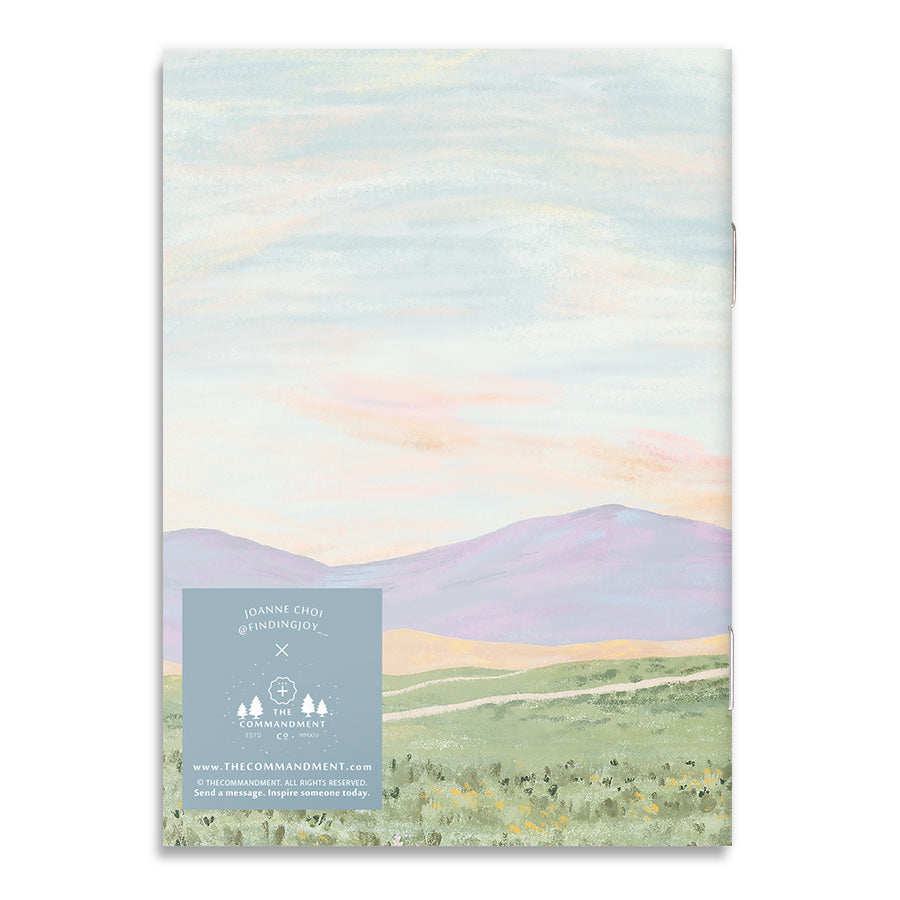 Back cover of A6 notebook featuring a pastel landscape, artist attribution, and an inspirational message promoting hope and faith