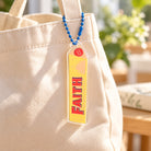 Faith Mountain Chocolate acrylic keychain hanging from a cream canvas tote bag