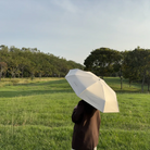 Person holding a cream-colored umbrella with the phrase “Enjoy today in the love of God” printed on it, standing in a green field under a clear sky, Christian gift from The Commandment Co.