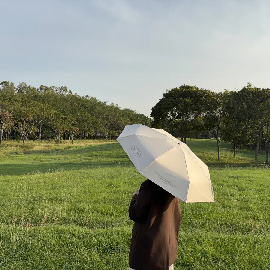 Person holding a cream-colored umbrella with the phrase “Enjoy today in the love of God” printed on it, standing in a green field under a clear sky, Christian gift from The Commandment Co.
