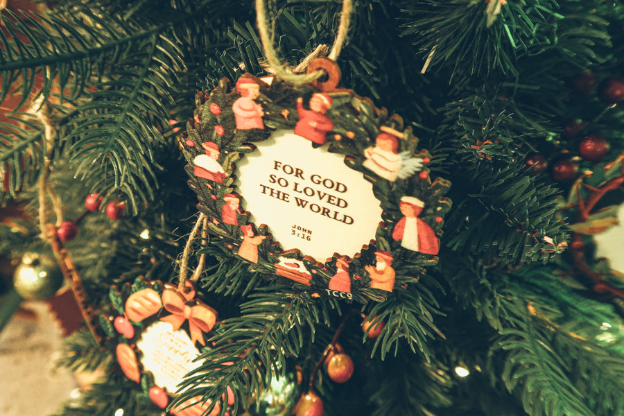 Close-up of a 'For God So Loved the World' Christmas ornament with a Bible verse, beautifully hanging on a decorated Christmas tree.