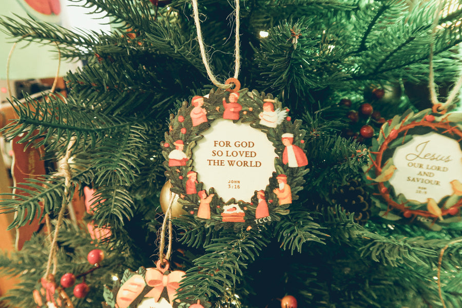 Beautiful 'For God So Loved the World' ornament featuring a Bible verse, hanging on a decorated Christmas tree with festive greenery.