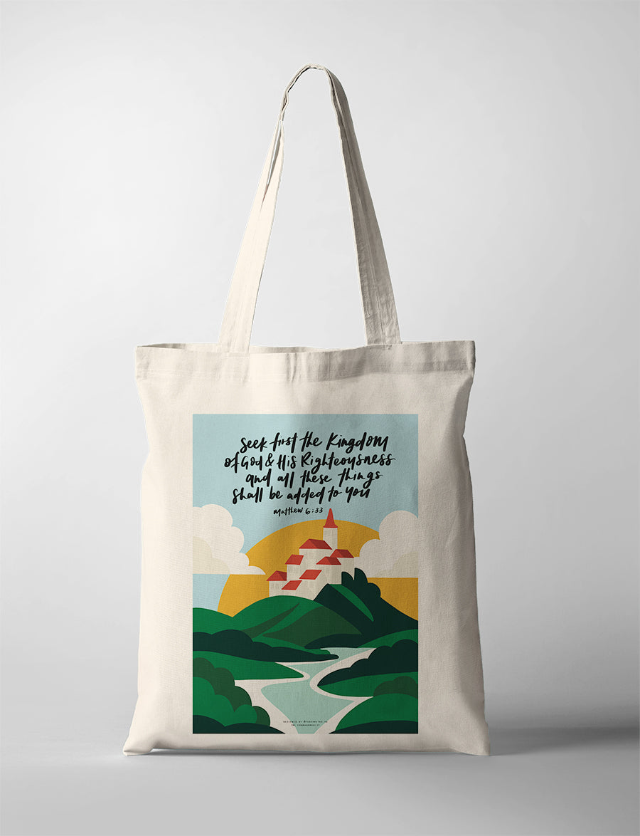 Christian canvas tote bag with “Seek first the kingdom of God” Matthew 6:33 verse, illustrated hills, winding path, and village artwork, designed by Fouronetwo.sg in collaboration with The Commandment Co.