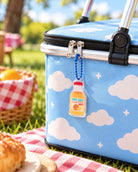 Fruit of the Spirit orange juice bottle acrylic keychain with blue bead chain on a cloud-patterned picnic cooler.