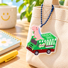 Fueled by Grace dinosaur malt beverage truck acrylic keychain hanging from a cream canvas tote bag.