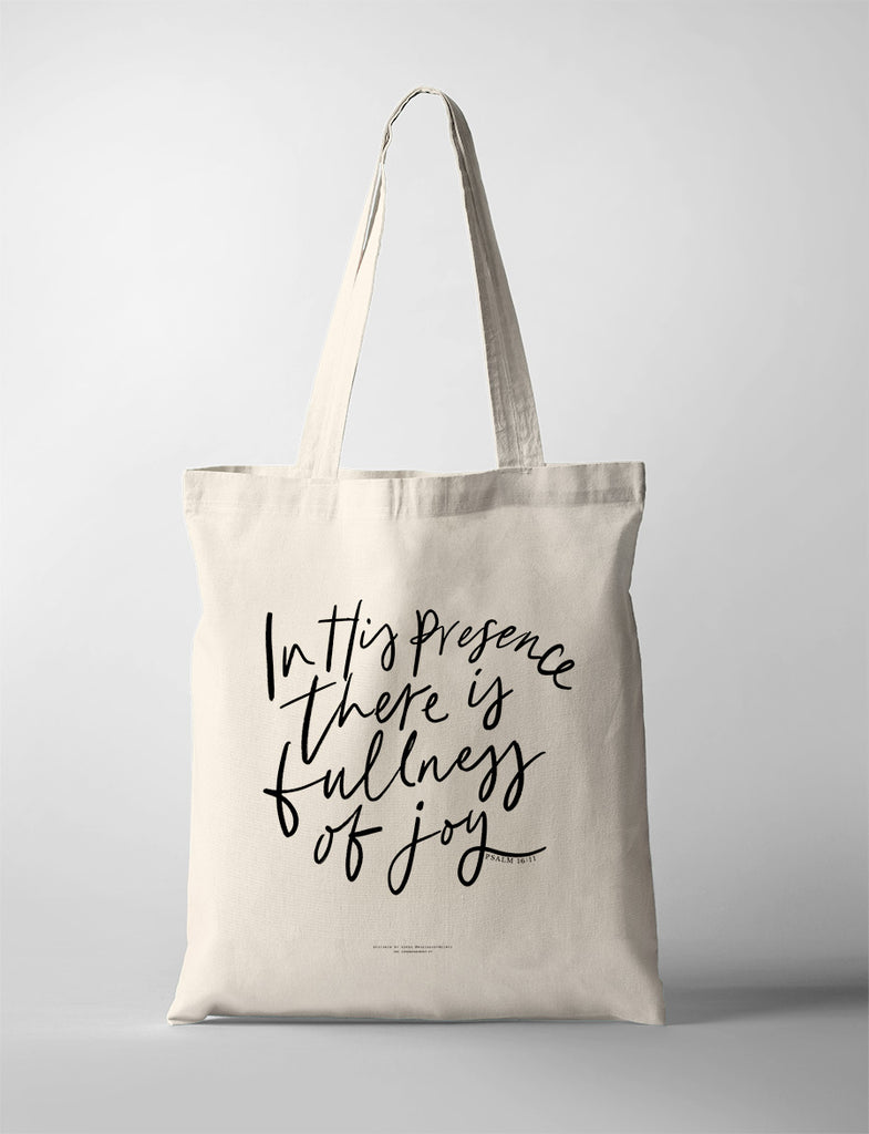 Beige tote bag with the words 'In His presence there is fullness of joy' from Psalm 16:11 printed in black handwritten-style script on the front.