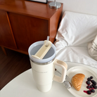 Cream insulated cup with the words "God has you in His heart" on a white table beside a plate of pastry and berries, creating a cozy and uplifting Christian gift scene that reflects simple happiness from Jincha God