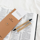 God is Love Pen Set with Bookmark placed on an open Bible, featuring uplifting messages and kraft packaging that reads "Hey! He loves you."