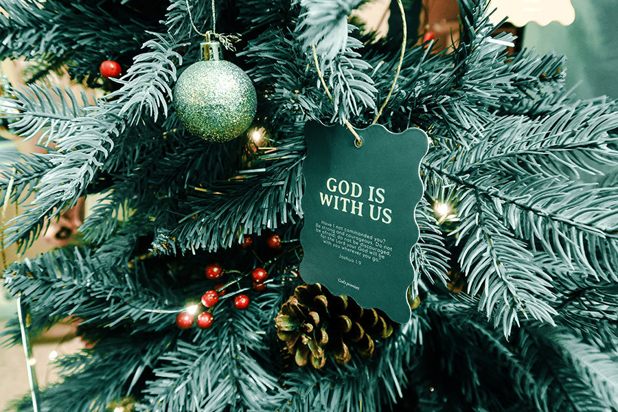 Christian Christmas tree hanging ornament featuring the Bible verse 'God Is With Us' from Joshua 1:9, with a green scalloped design, pinecones, and festive decorations.