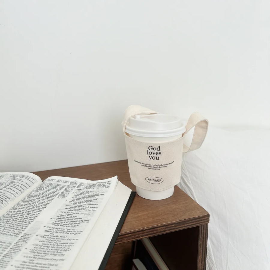 Eco-friendly reusable cup holder with "God loves you" and Jeremiah 31:3 Bible verse, perfect Christian gift for coffee lovers, shown on a bedside table with an open Bible.