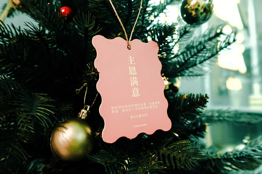 Christian Christmas tree hanging ornament featuring the Bible verse 'God Provides Abundantly' from Philippians 4:19, with a pink scalloped design and gold ornaments in the background.