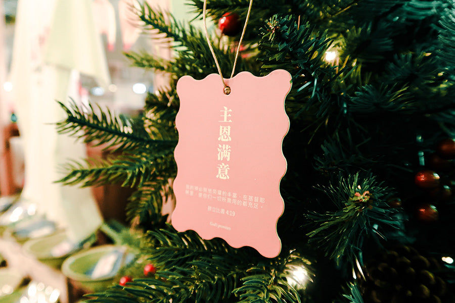 Christian Christmas tree hanging ornament featuring the Bible verse 'God Provides Abundantly' from Philippians 4:19, with a pink scalloped design hanging on a decorated tree.