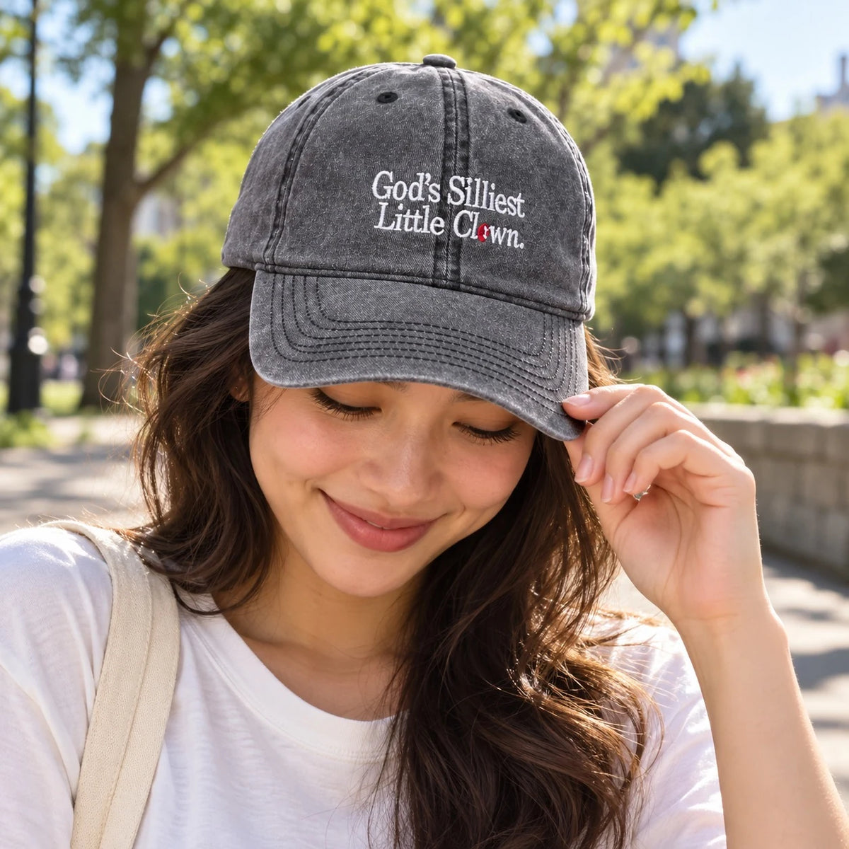 Lifestyle photograph of a woman wearing the washed-grey God's Silliest Little Clown embroidered cap outdoors.