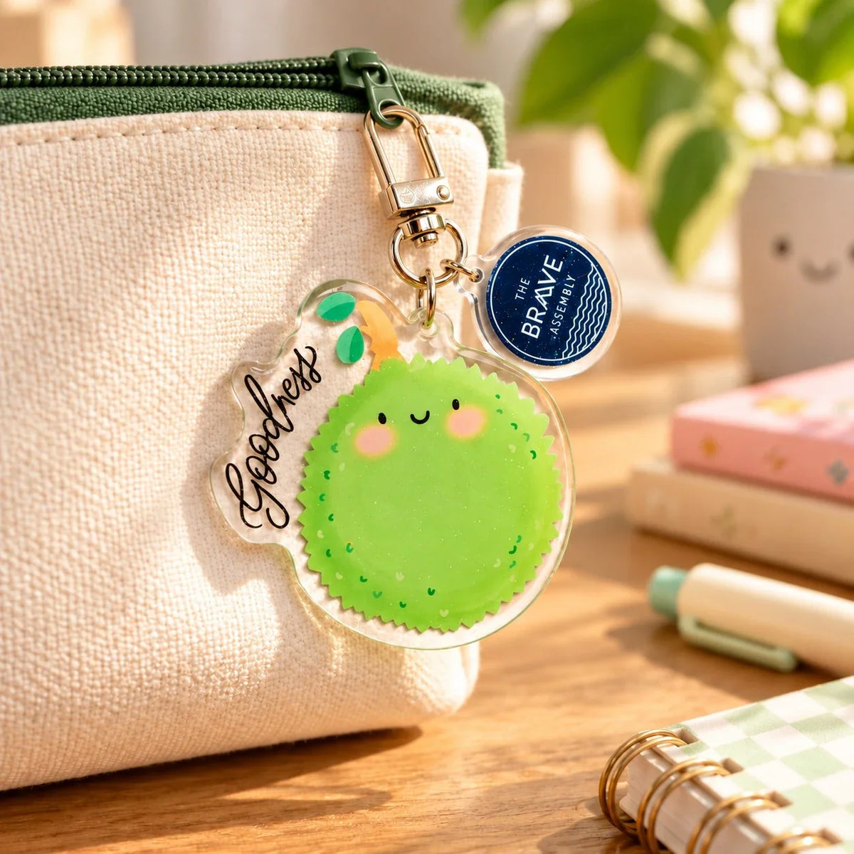 Smiling Goodness Durian acrylic keychain clipped to a beige and green canvas pouch.