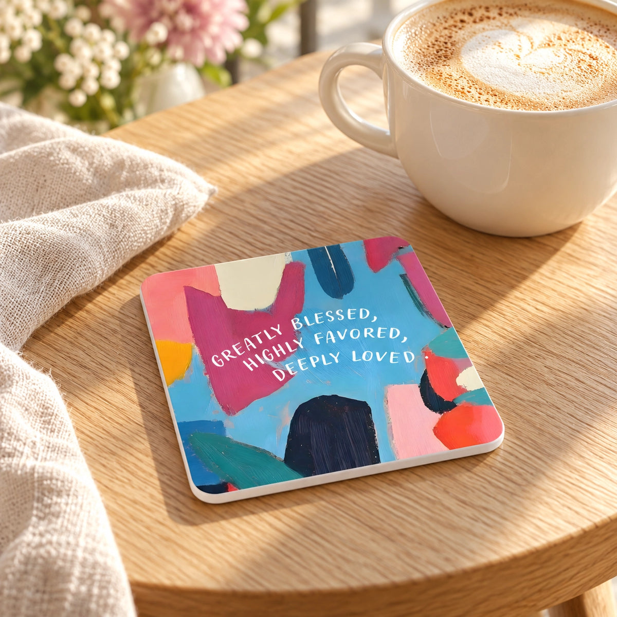 Greatly Blessed Highly Favored Deeply Loved Christian coaster styled on a warm wooden table beside coffee