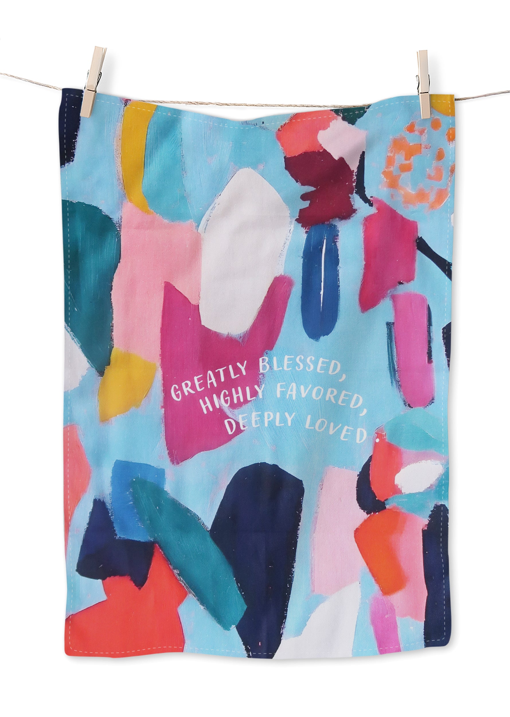 Colorful abstract art tea towel with pastel blues, pinks, and orange shapes, featuring the curved white text “Greatly Blessed, Highly Favored, Deeply Loved” on a light blue background, hanging on a clothesline.