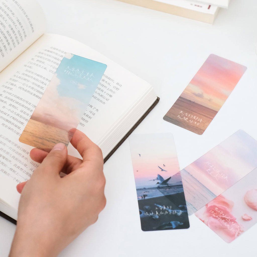 A person placing a Christian-themed bookmark with a sunset design into an open book, surrounded by other inspirational bookmarks featuring Bible quotes and faith-based designs