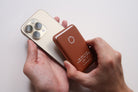 A pair of hands attaching a Brown Leather Magsafe Wallet to the back of a mobile phone