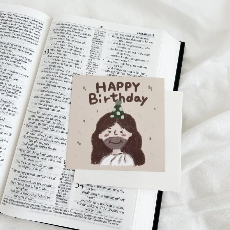 "Happy Birthday" postcard featuring a cute illustration of Jesus with a party hat, placed on an open Bible.