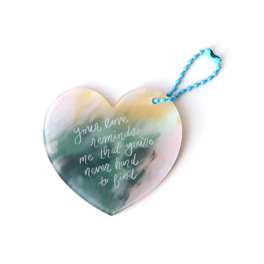 Heart-shaped Christian keychain featuring the inspirational quote 'Your love reminds me that you're never hard to find' with a watercolor-style background and a blue chain.