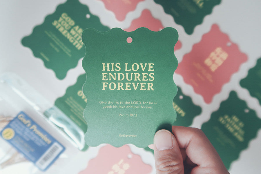 Christian Christmas tree hanging ornament or bookmark with the Bible verse 'His Love Endures Forever' from Psalm 107:1, featuring a green design held in hand.