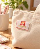 His Mercy Endures Forever LOVE SUPERMARKET pin with red and cream packaging design on a canvas bag.