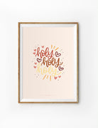 A faith-based poster featuring the words 'Holy, Holy, Holy' in warm, earthy typography with red and gold hand-drawn hearts and decorative dots. The minimalist Christian wall art has a soft beige background, framed in a simple wooden frame, making it a perfect decor piece for a faith-inspired home or prayer space.