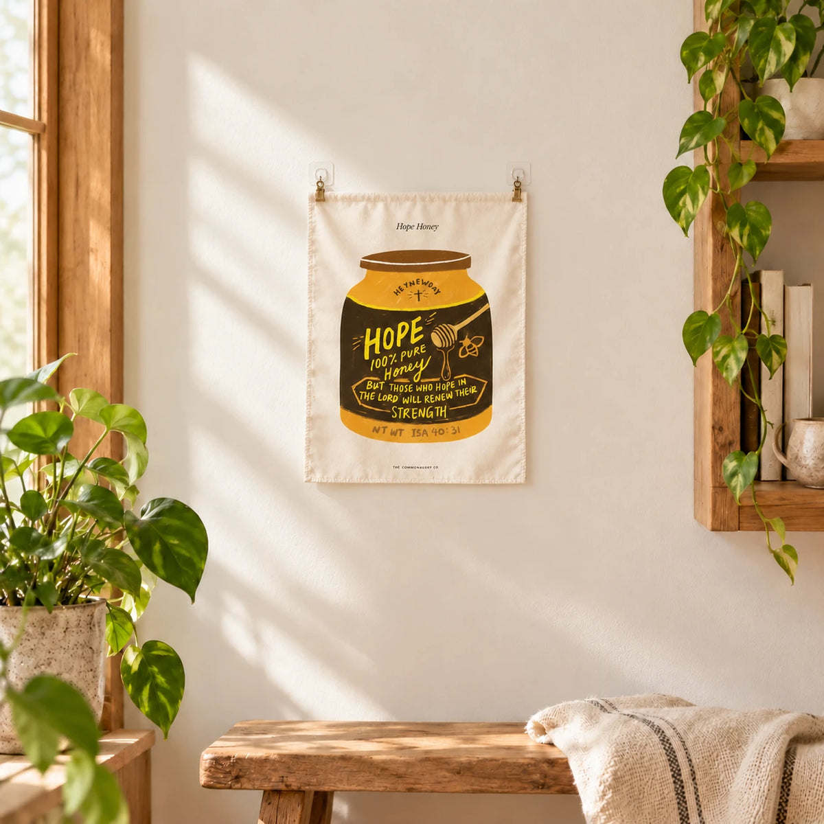 Hope Honey wall tapestry displayed on a sunlit wall, held with two small adhesive clips above a wooden bench
