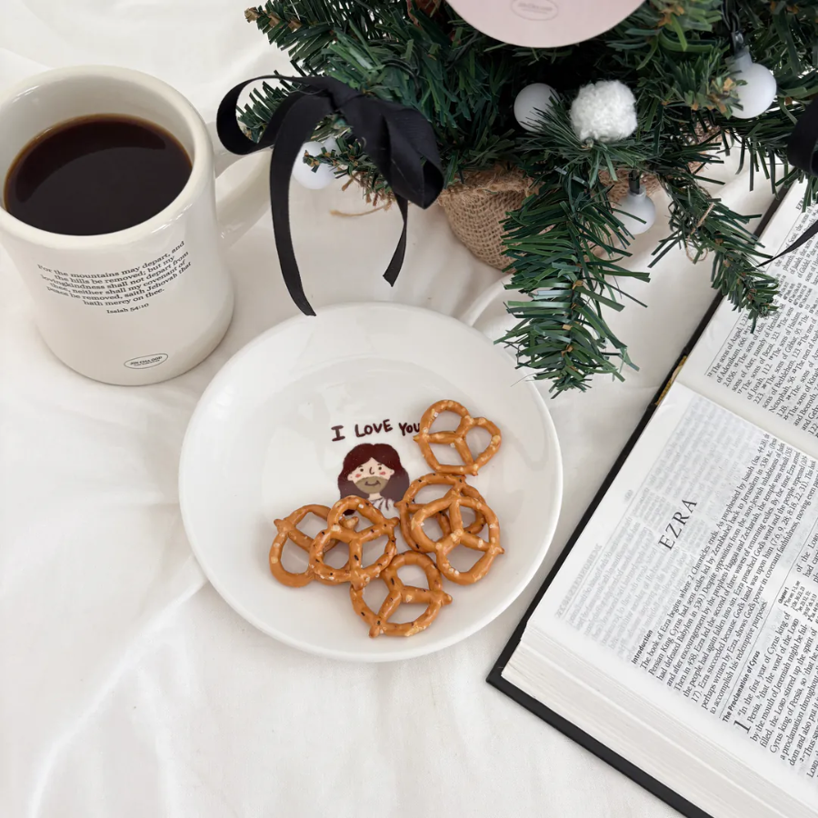 I Love You" dessert plate featuring a cute illustration of Jesus, topped with pretzels, beside a coffee mug, Bible, and Christmas tree, sharing a message of love and simple happiness from Jincha God.