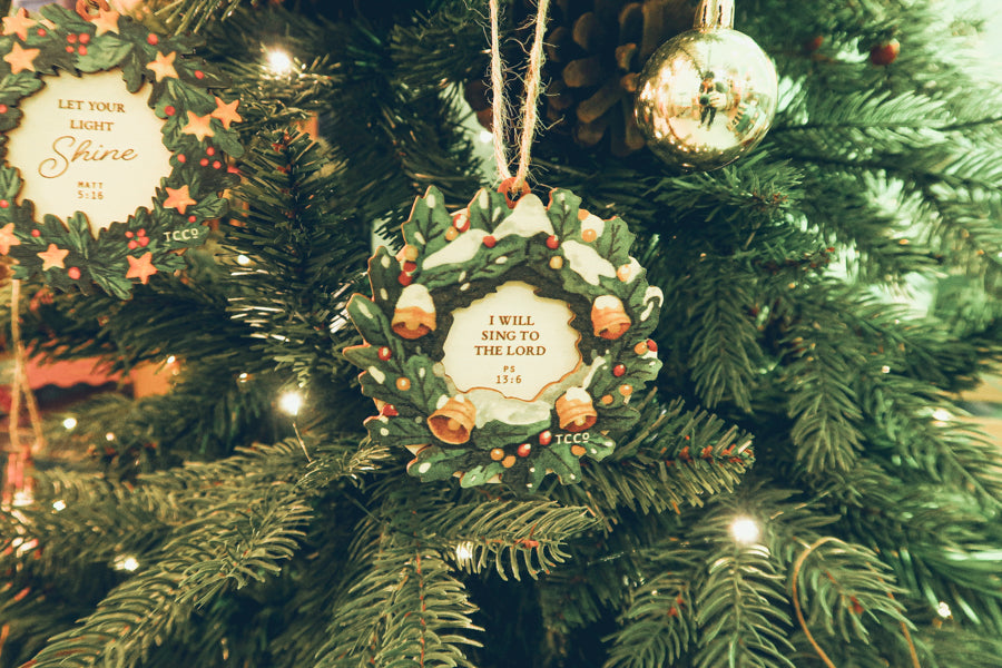 'I Will Sing to the Lord' Christmas ornament with a festive wreath design, hanging beautifully on a lit Christmas tree adorned with pine needles and decorations.