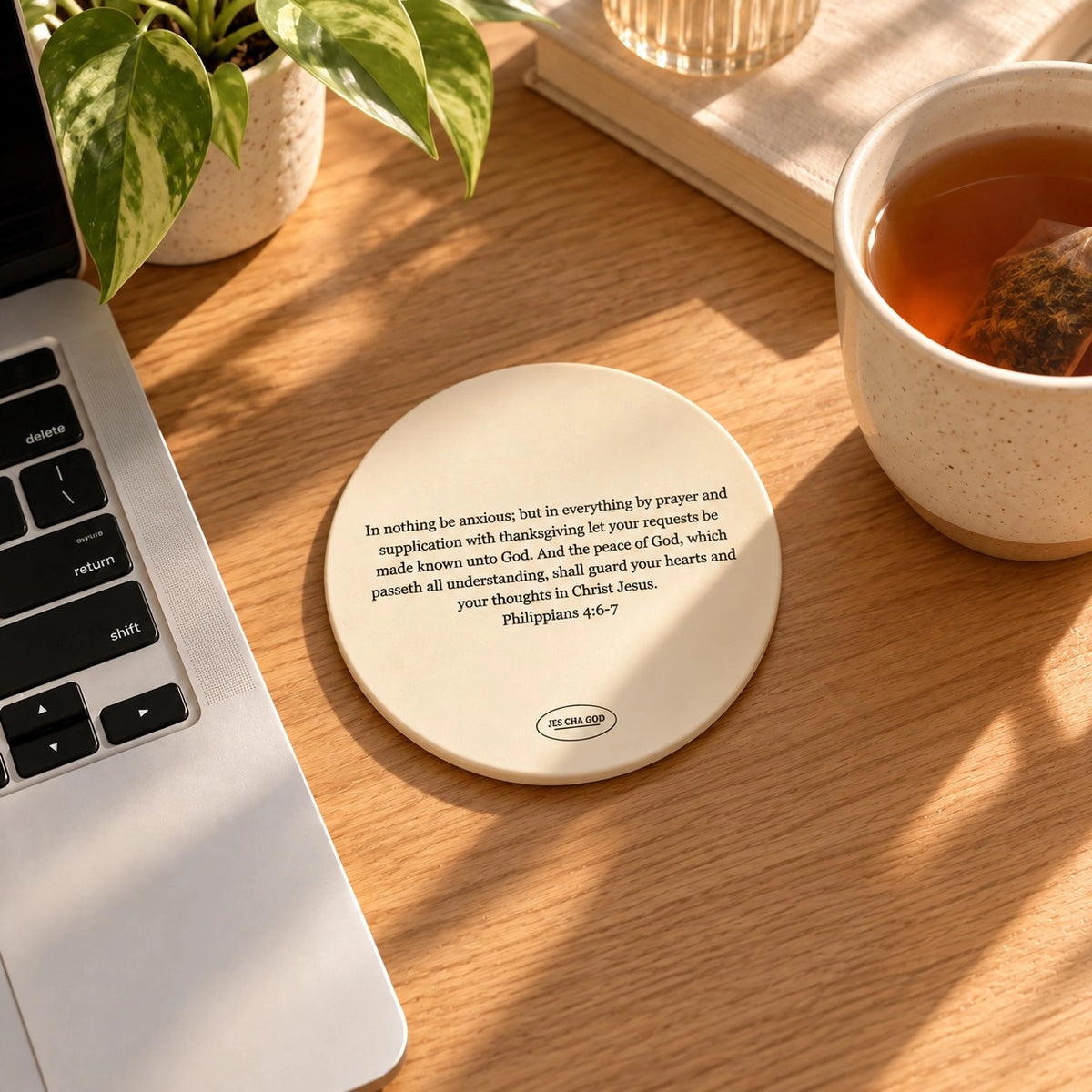 Philippians 4:6–7 ceramic coaster beside a laptop and cup of tea on a sunlit wooden desk.