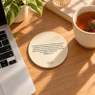 Philippians 4:6–7 ceramic coaster beside a laptop and cup of tea on a sunlit wooden desk.