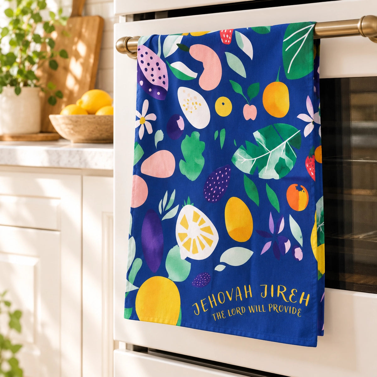 Jehovah Jireh Christian tea towel with colourful fruit pattern hanging in a bright sunlit kitchen