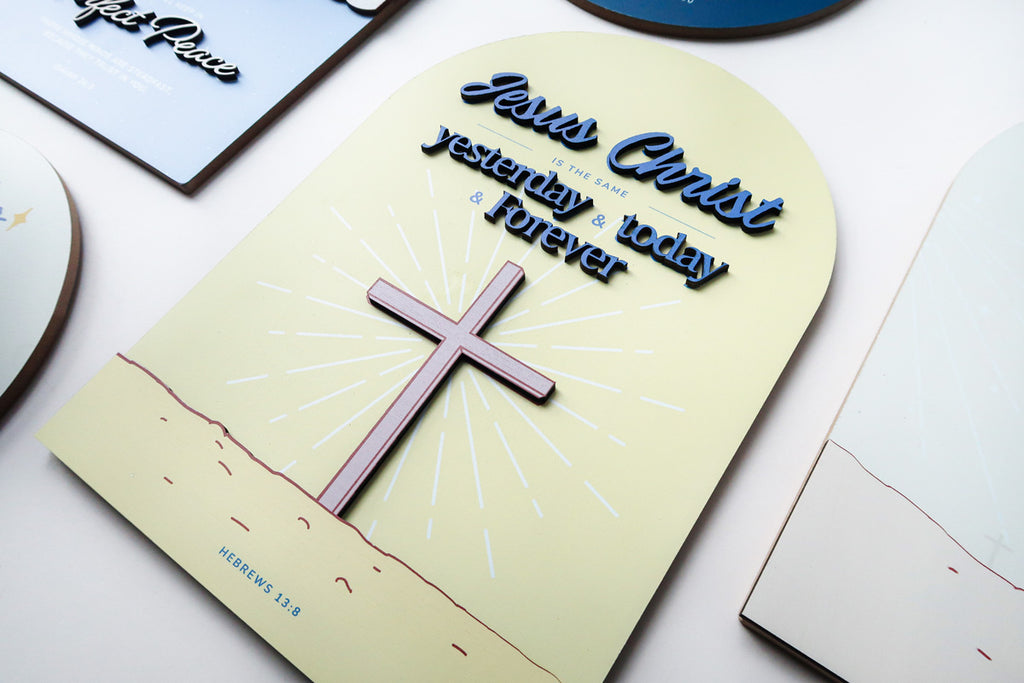 Angled close-up of a 3D wooden Christian poster featuring the phrase 'Jesus Christ is the same yesterday, today, and forever,' with a cross illustration and the Bible verse Hebrews 13:8.